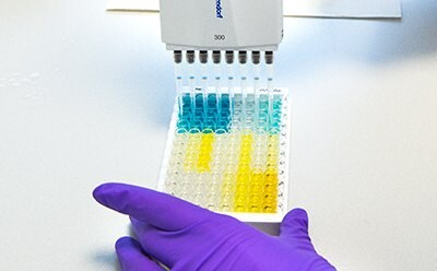 Pyrogen Testing Methods - What is a Pyrogen? A scientist wearing full PPE observes a sample on a microscope.
